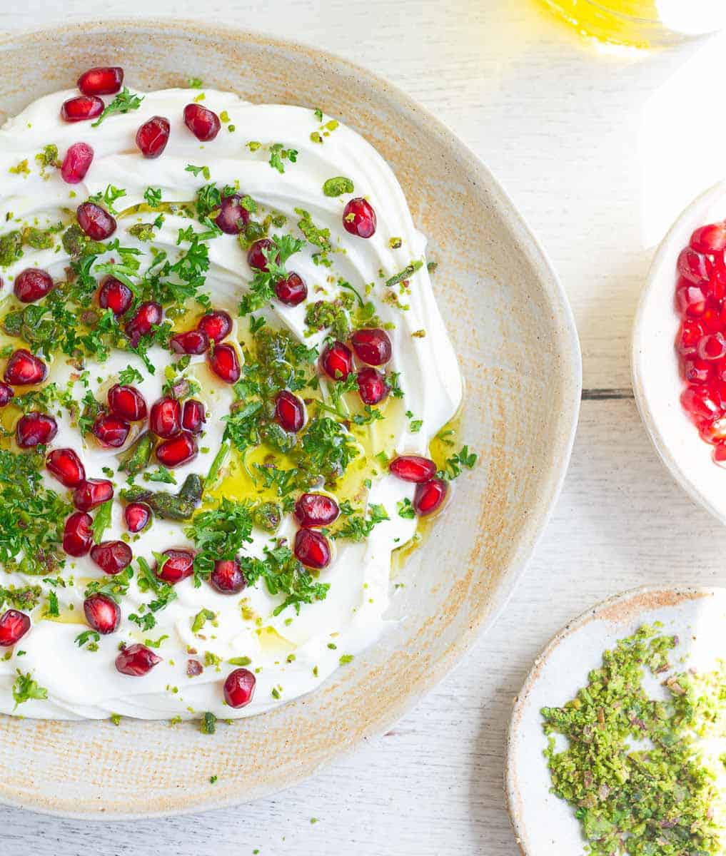 Dip with pomegranate arils, parsley and olive oil in a ceramic bowl.
