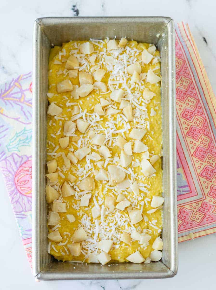 Mango Bread batter with macadamia nuts and shredded coconut on top in a loaf tin.