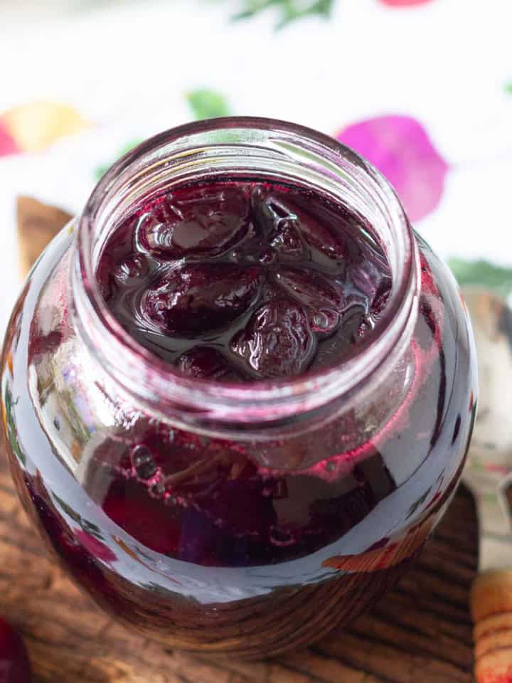 A jar with cherry jam on a wooden surface with a spoon on the side.