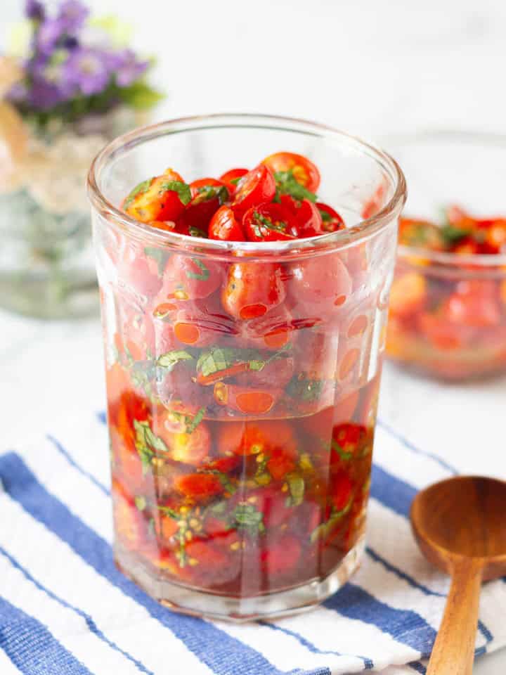 marinated cherry tomatoes in glass jar with a wooden spoon.