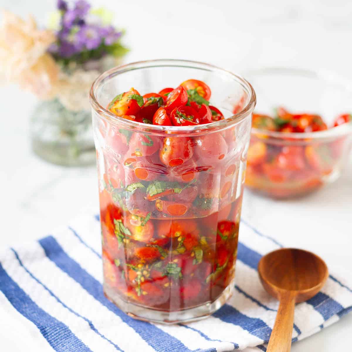 marinated cherry tomatoes in glass jar with a wooden spoon.