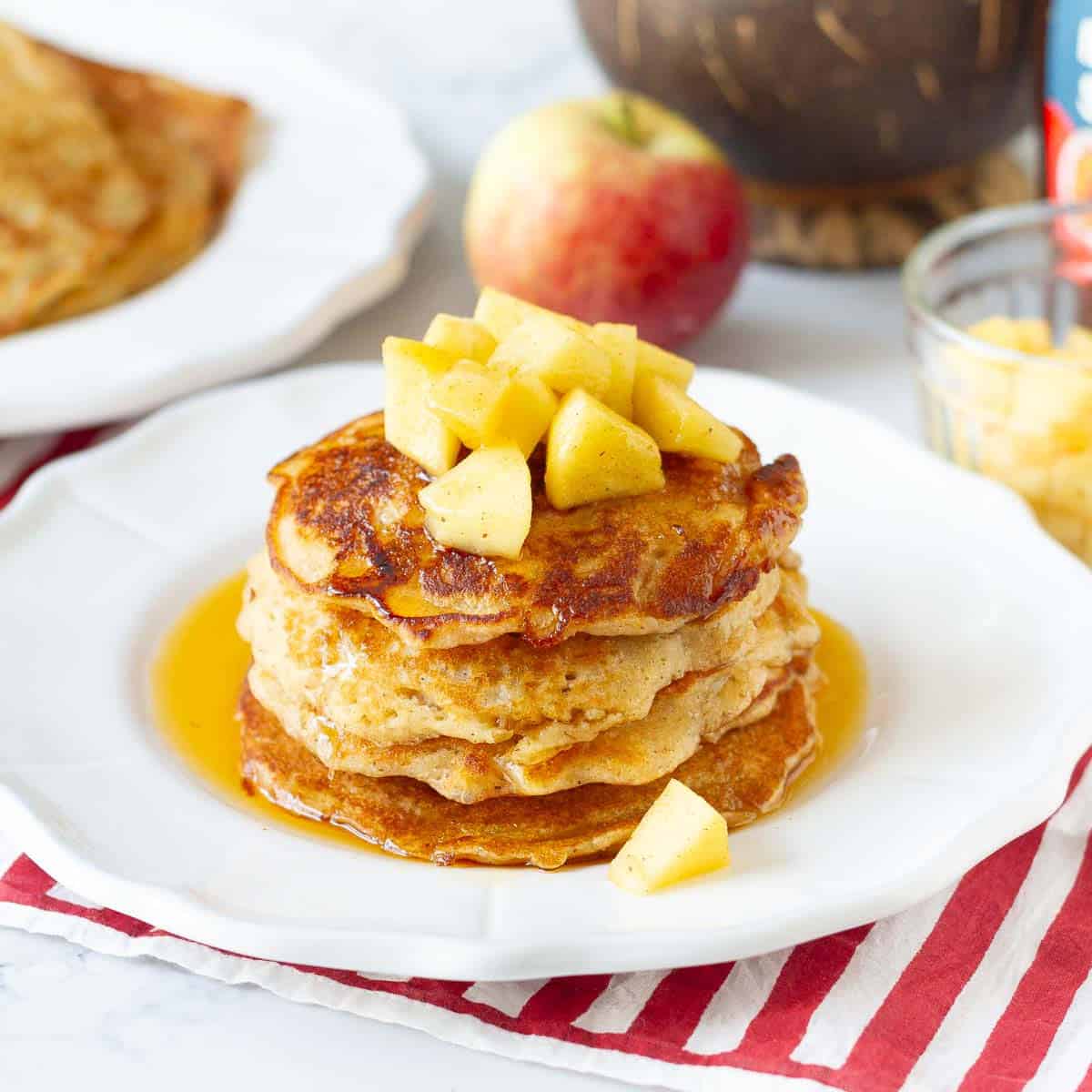 A stack of apple pancakes topped with sauteed apples and maple syrup on a plate.