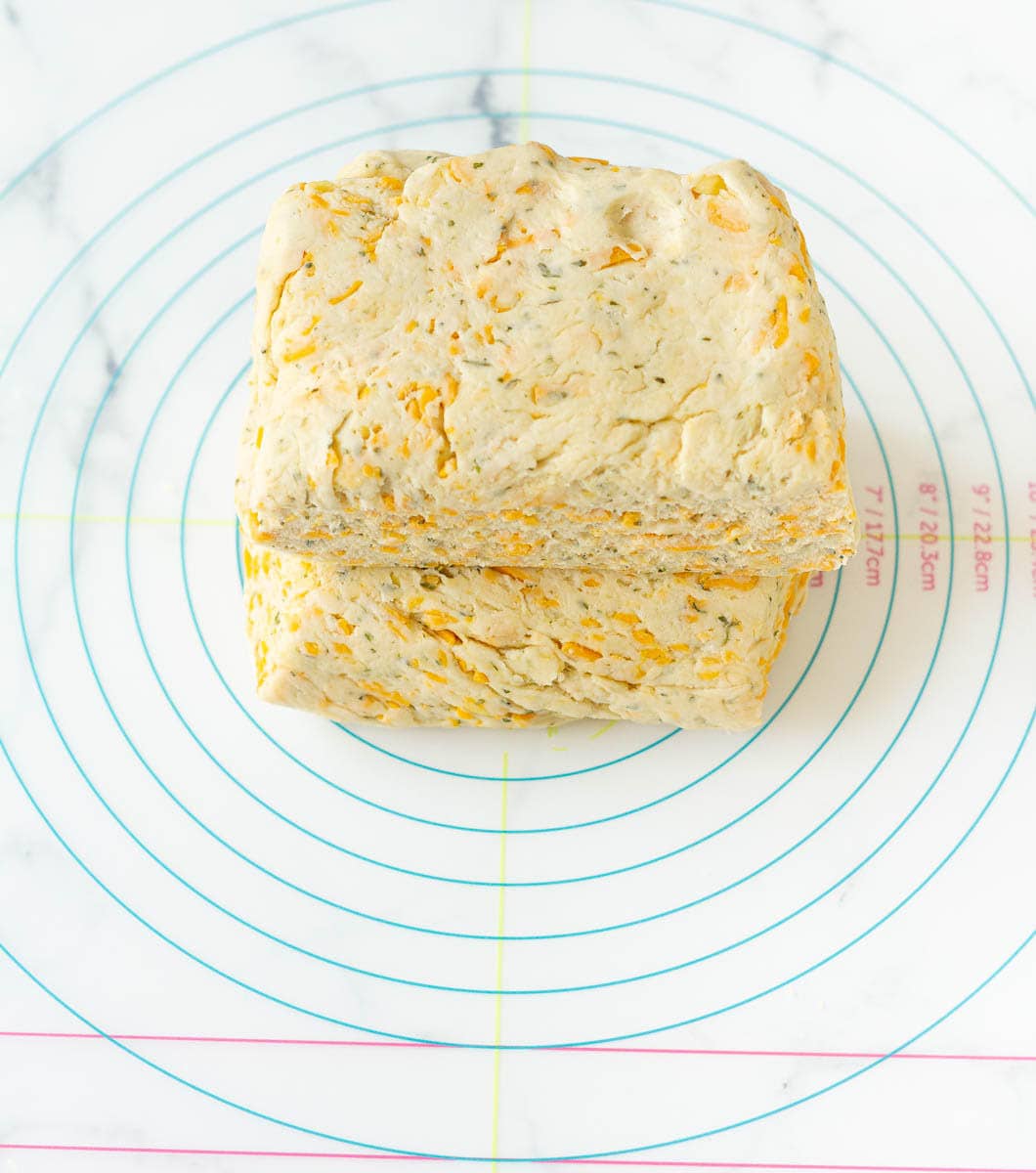 Cheese scone dough halves stacked on top of each other placed on a silicon mat