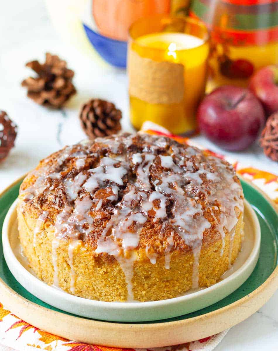 Cinnamon Swirl Apple Cake on a cake platter with apples and candle in the background.