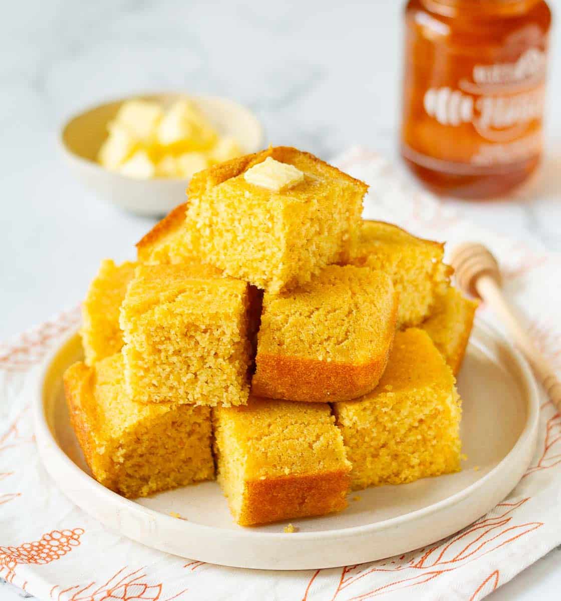 A plate of homemade cornbread squares stacked on each other.