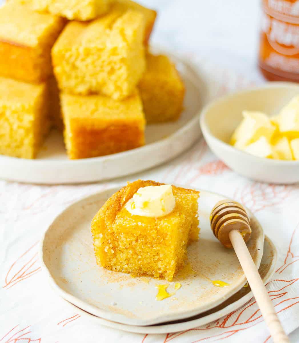 Cornbread slice on a plate, topped with honey and a piece of butter.