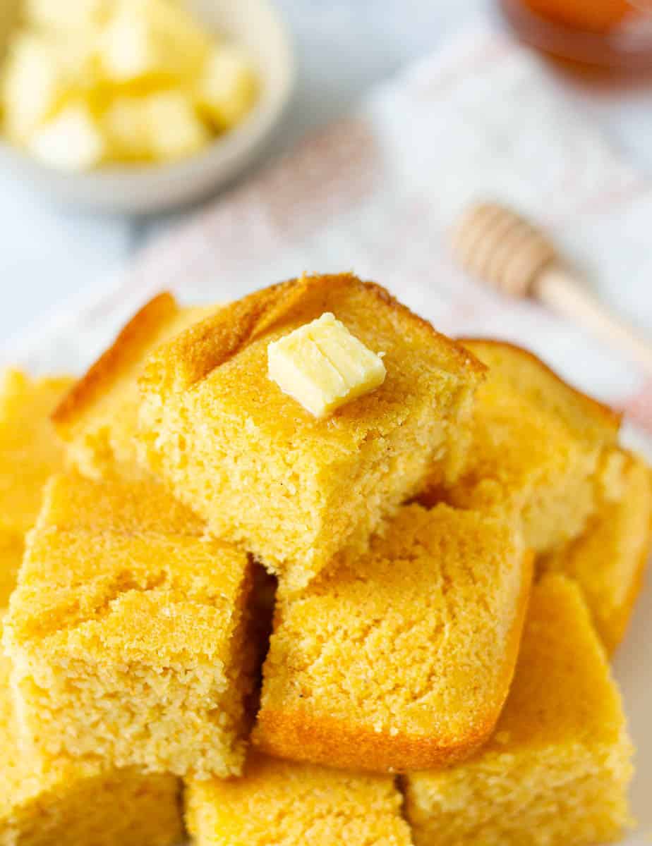 cornbread squares stacked on top of each other, with a piece of butter on top.