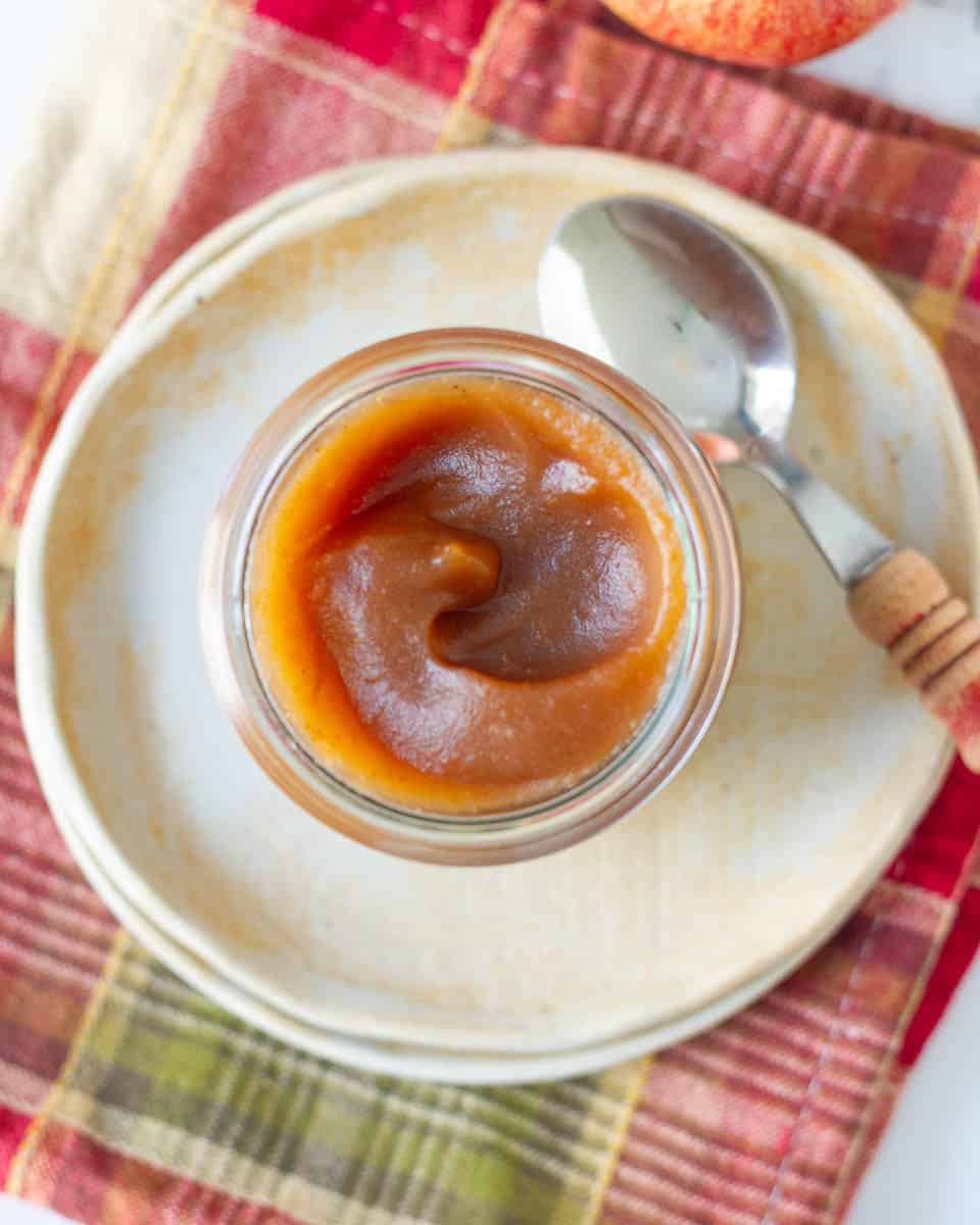 stovetop apple butter in a glass jar with spoon on a small plate.