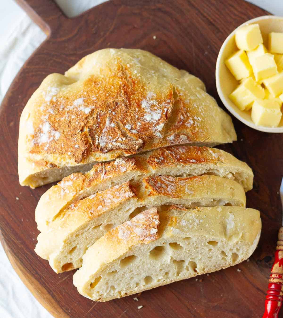 Half sliced loaf of bread on a wooden board with butter in a small dish.