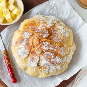 no knead Dutch oven bread on parchment paper with butter and butter knife.