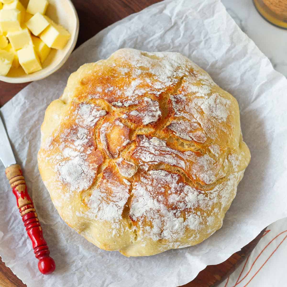 no knead Dutch oven bread on parchment paper with butter and butter knife.