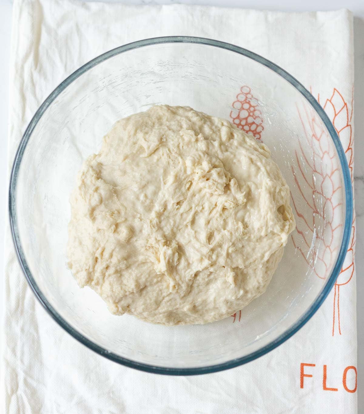 Flour, yeast, salt, water mixed into a shaggy dough in clear glass bowl.