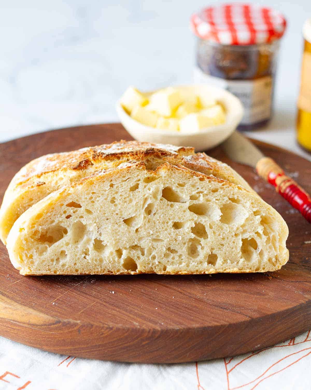 Slice of no knead bread on a wooden board with butter and butter knife.