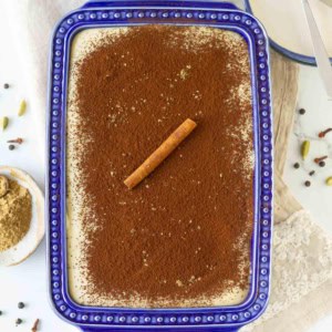 masala chai tiramisu in a blue dish with chai masala and other spices around.