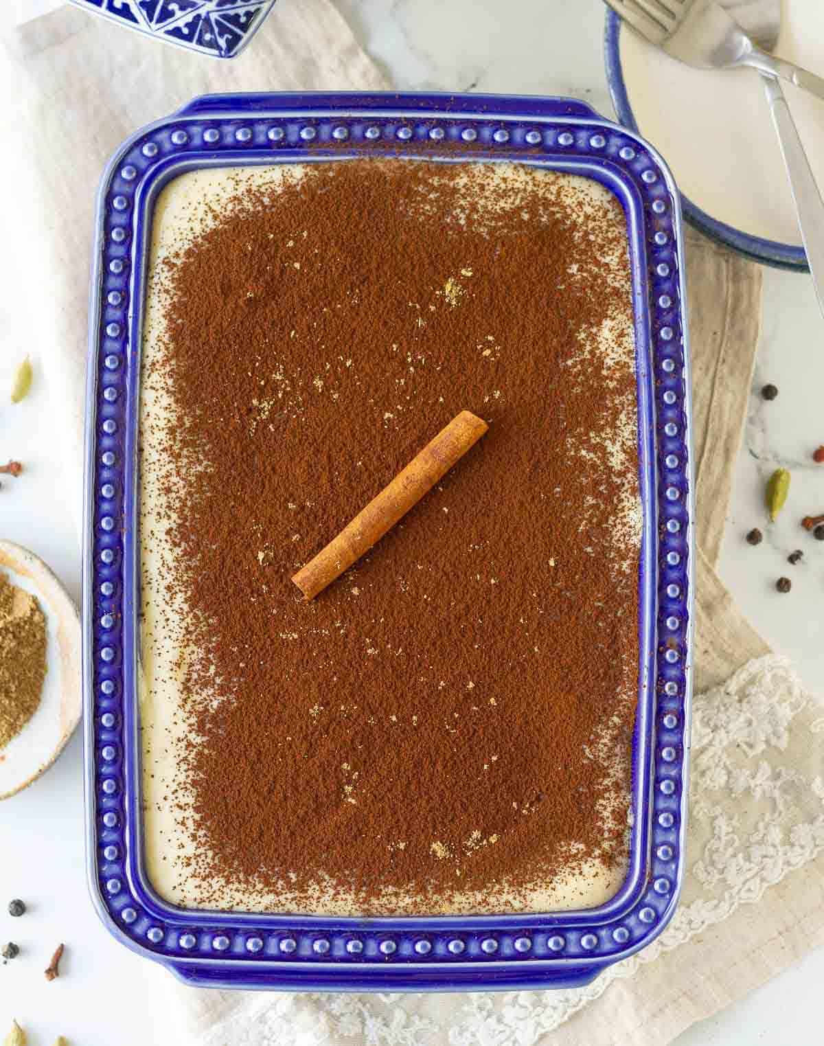 chai tiramisu in a blue dish with chai masala and other spices around.