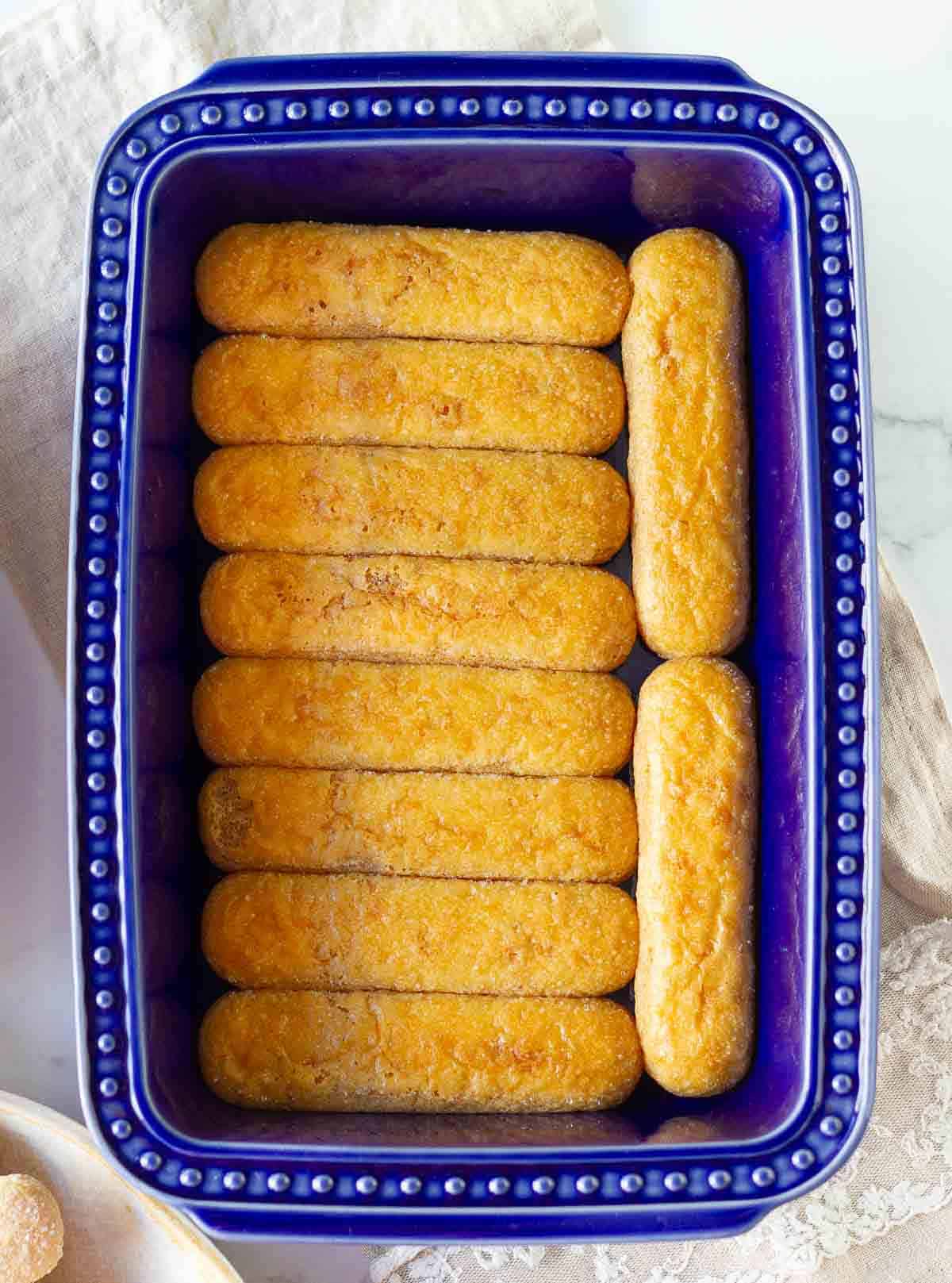 Chai soaked ladyfinger cookies layered in a blue dish.
