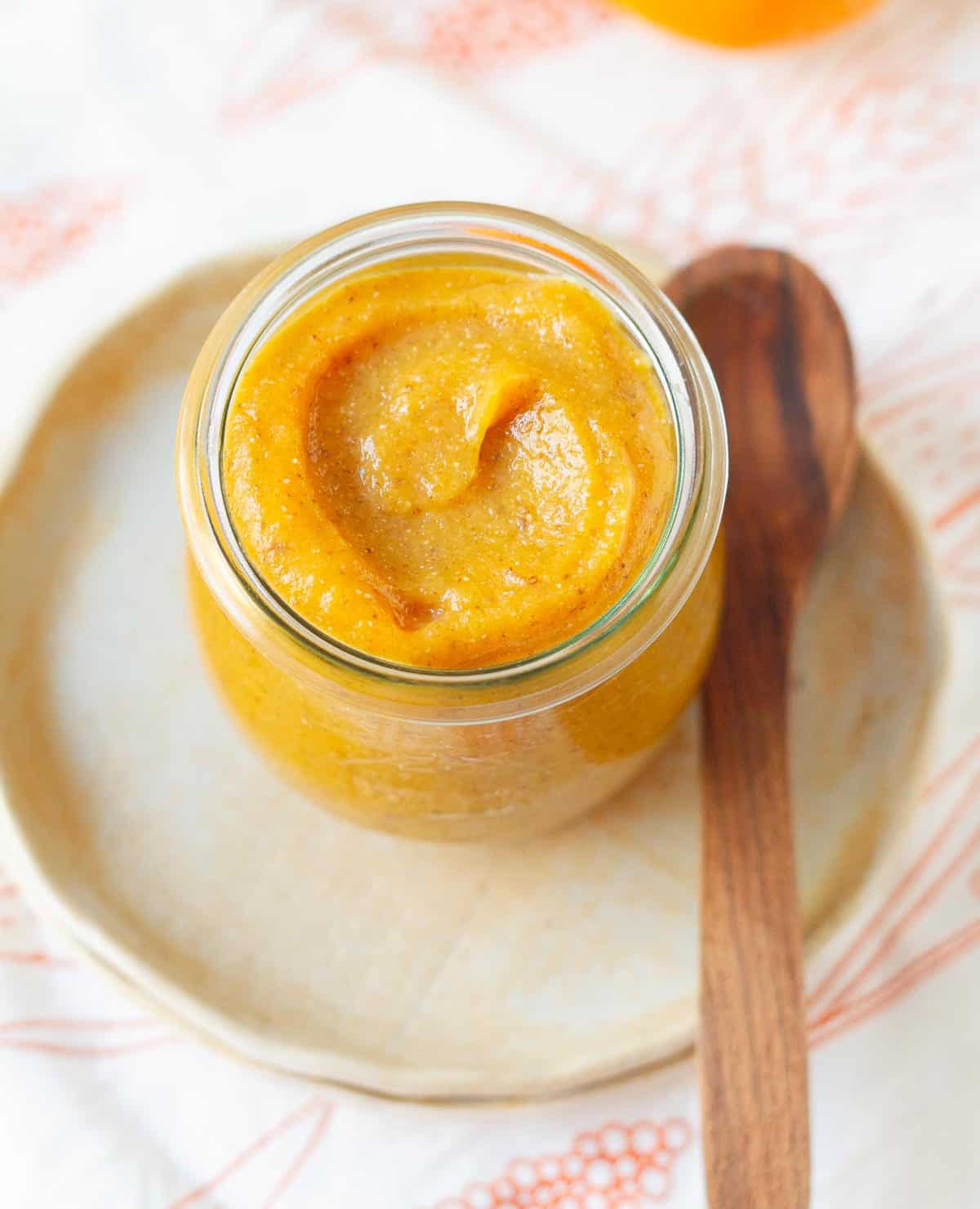 persimmon jam in a glass jar with a wooden spoon on a small plate.