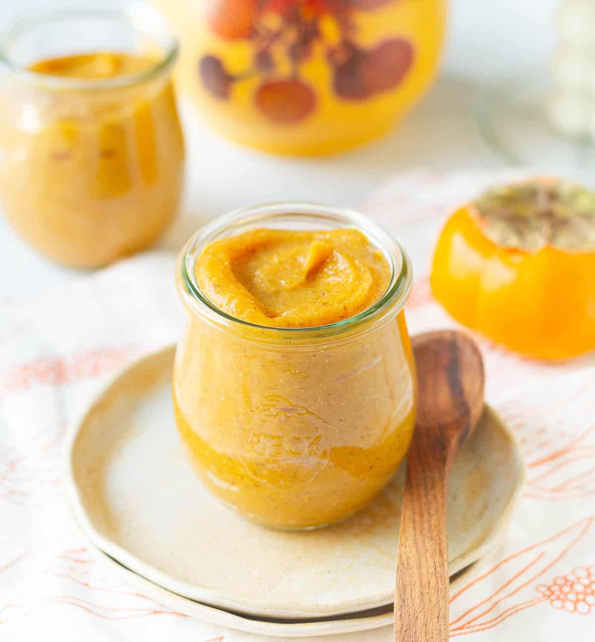 persimmon jam in a jar with a wooden spoon and ingredients in the background.
