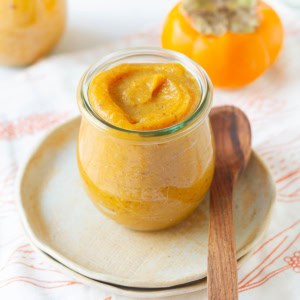 persimmon chia jam in a glass jar with a wooden spoon on a small plate.