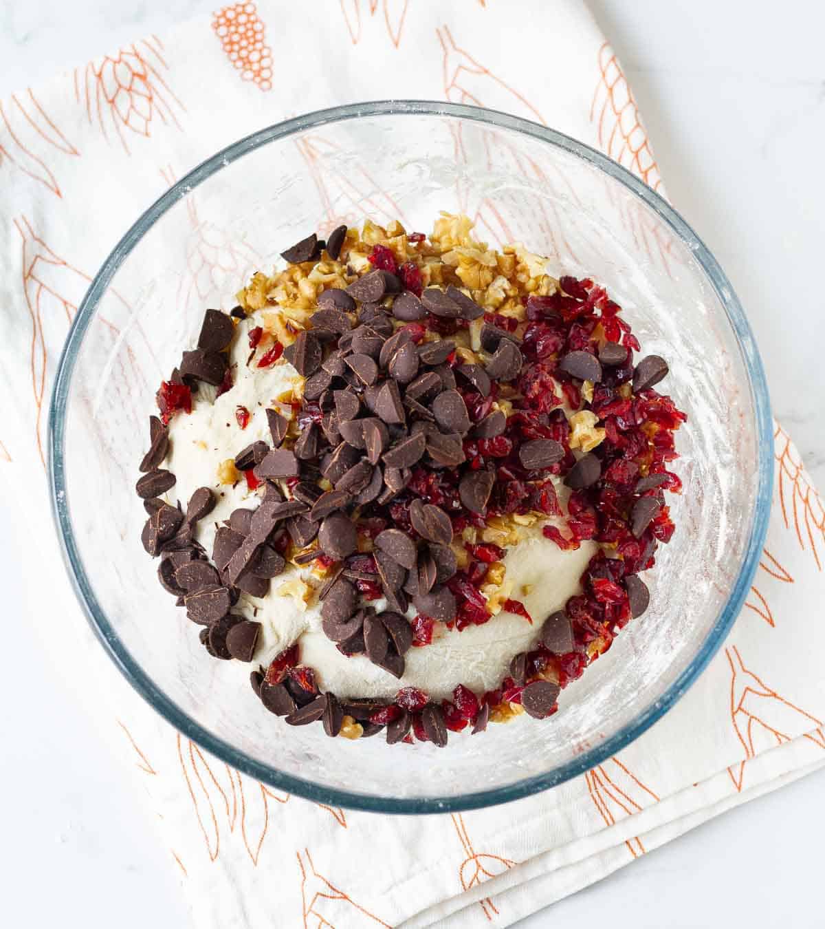 dried cranberries, walnuts, and chocolate chips on top of the proofed bread dough in a bowl.
