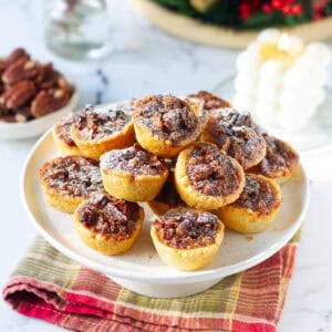 pecan tassies on a cake stand with a candle and pecans in the background.