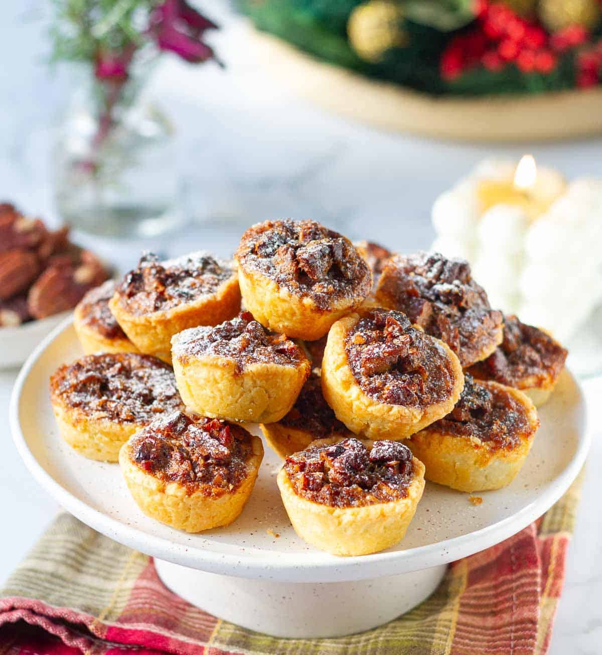 tassies on a cake stand with candles and christmas decor in the background.