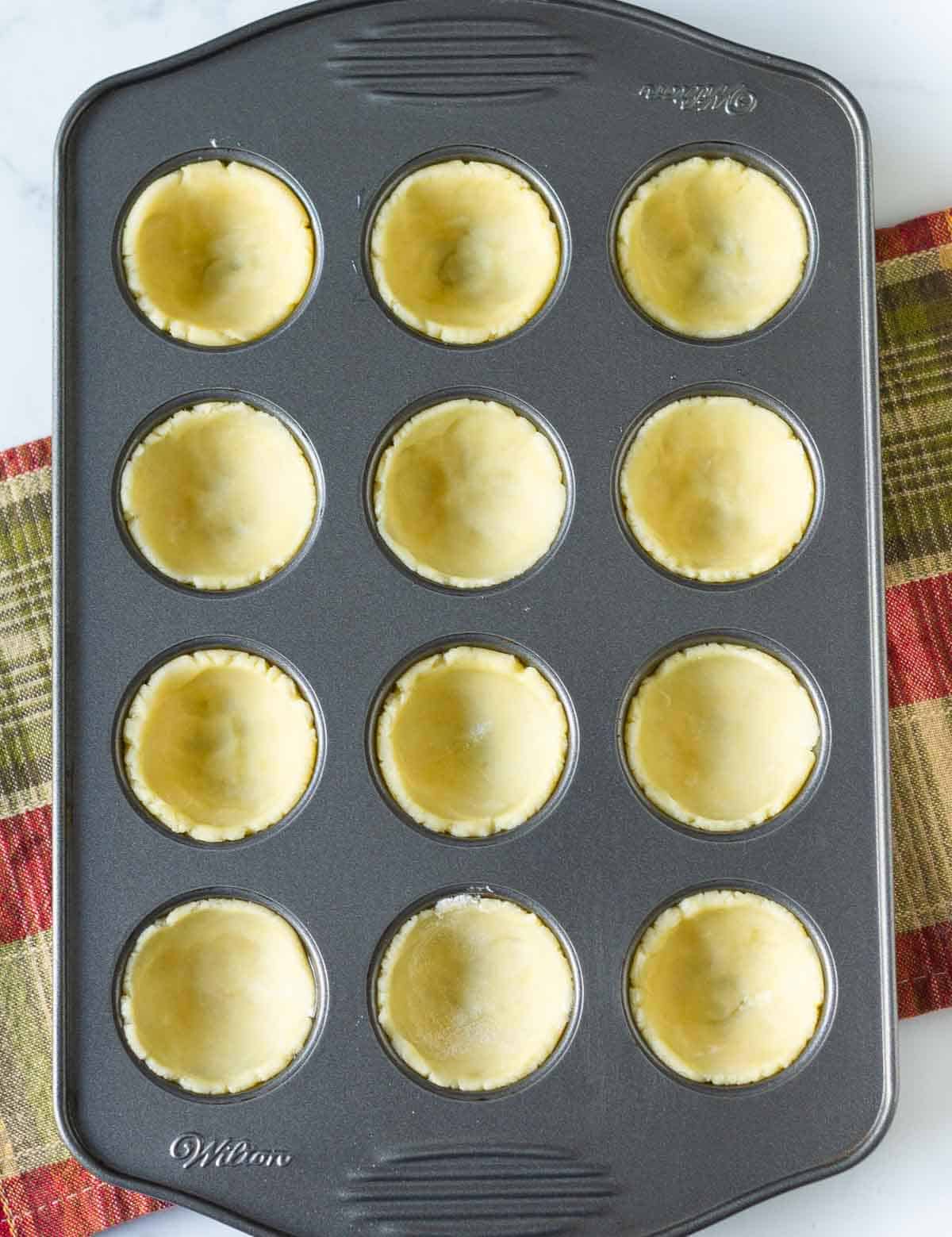 pressed dough in the cups of a mini muffin pan.