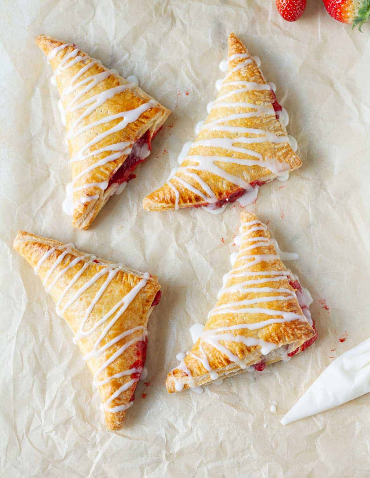 four turnovers with vanilla glaze on parchment paper.