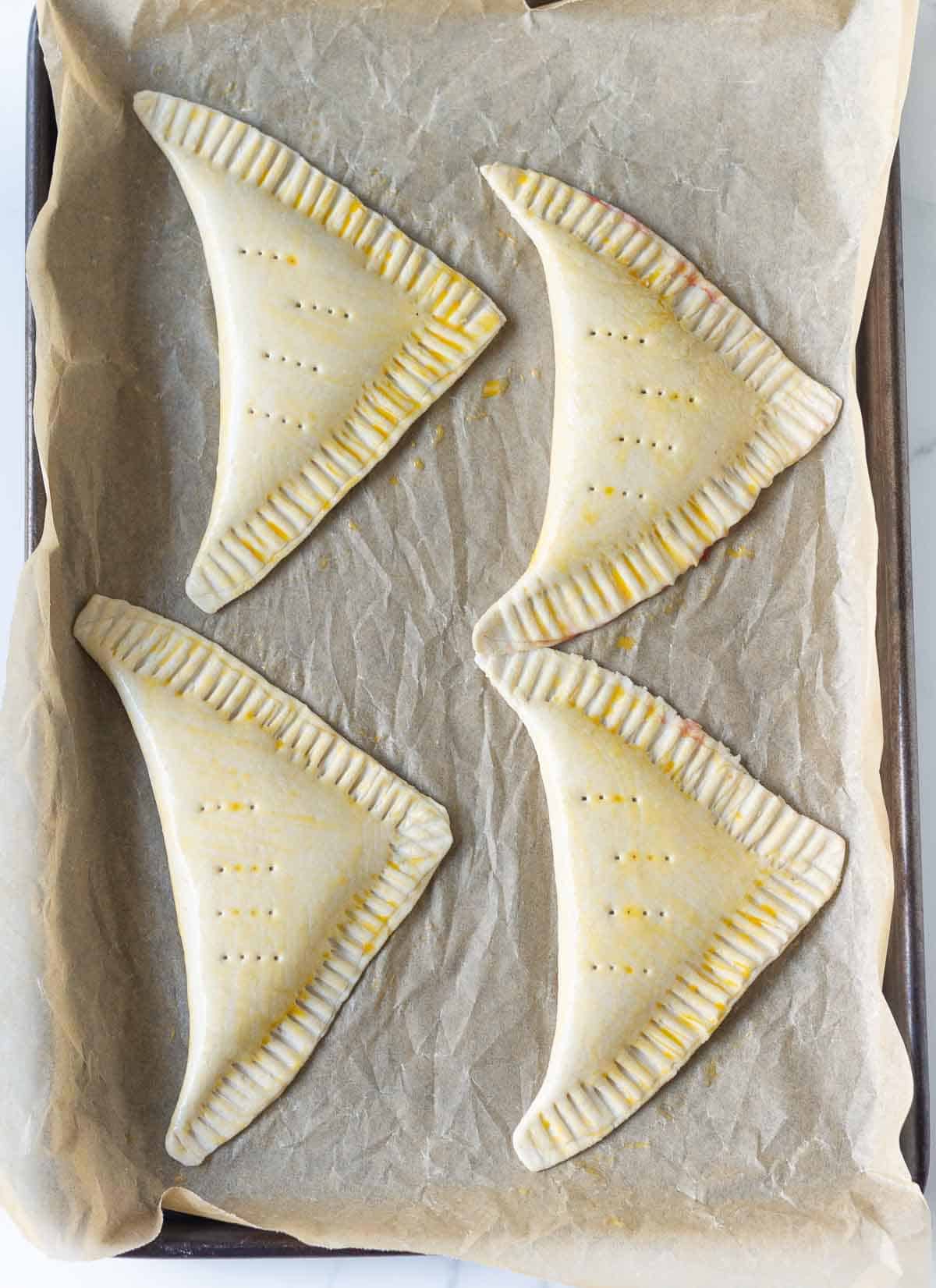 4 puff pastry turnovers with eggwash on parchment paper on a baking tray.