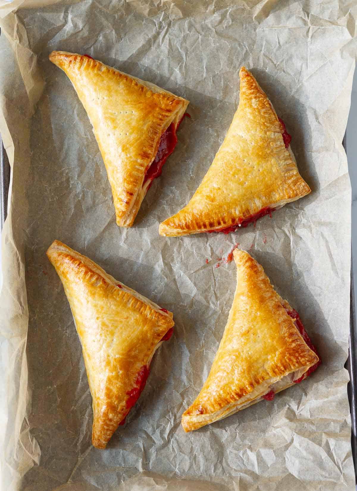 Four golden baked strawberry turnovers on parchment paper.
