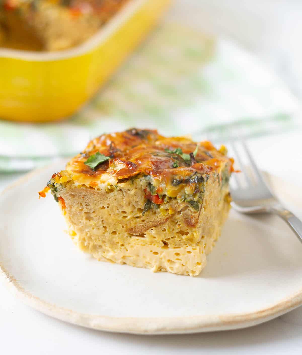 A slice of breakfast casserole on a plate with a fork on the side.