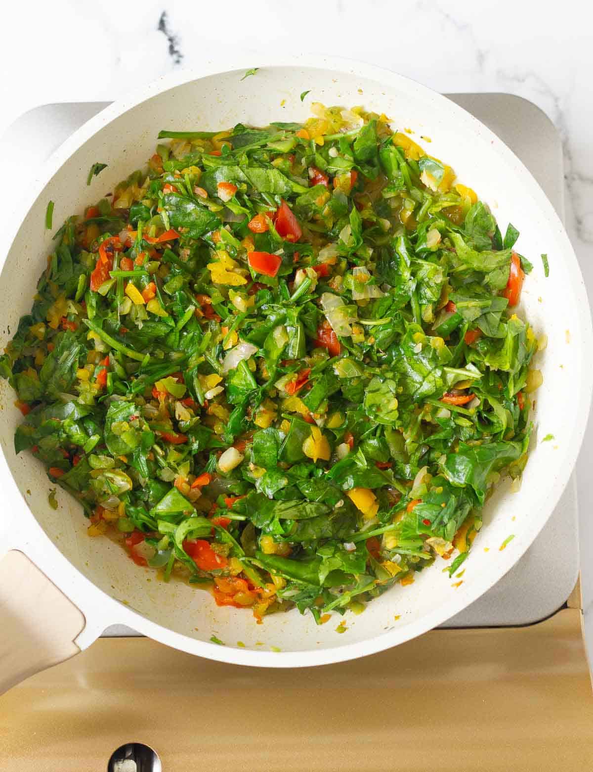chopped spinach on top of sauteed veggies in a saucepan.