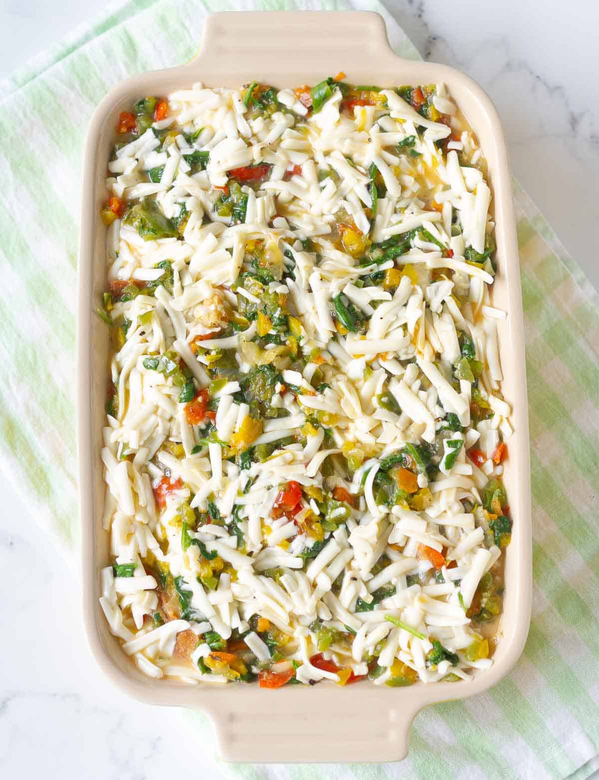 egg-cheese mixture on top of the veggies and bread in a casserole dish.