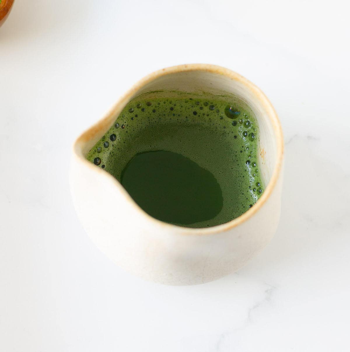 Matcha powder mixed with water in a small ceramic creamer.