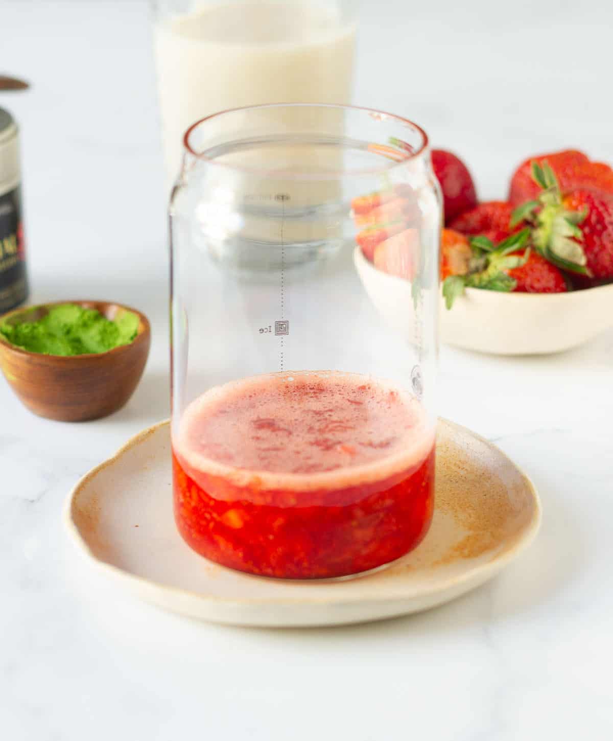 chopped, mashed strawberries in a glass with ingredients in the background.