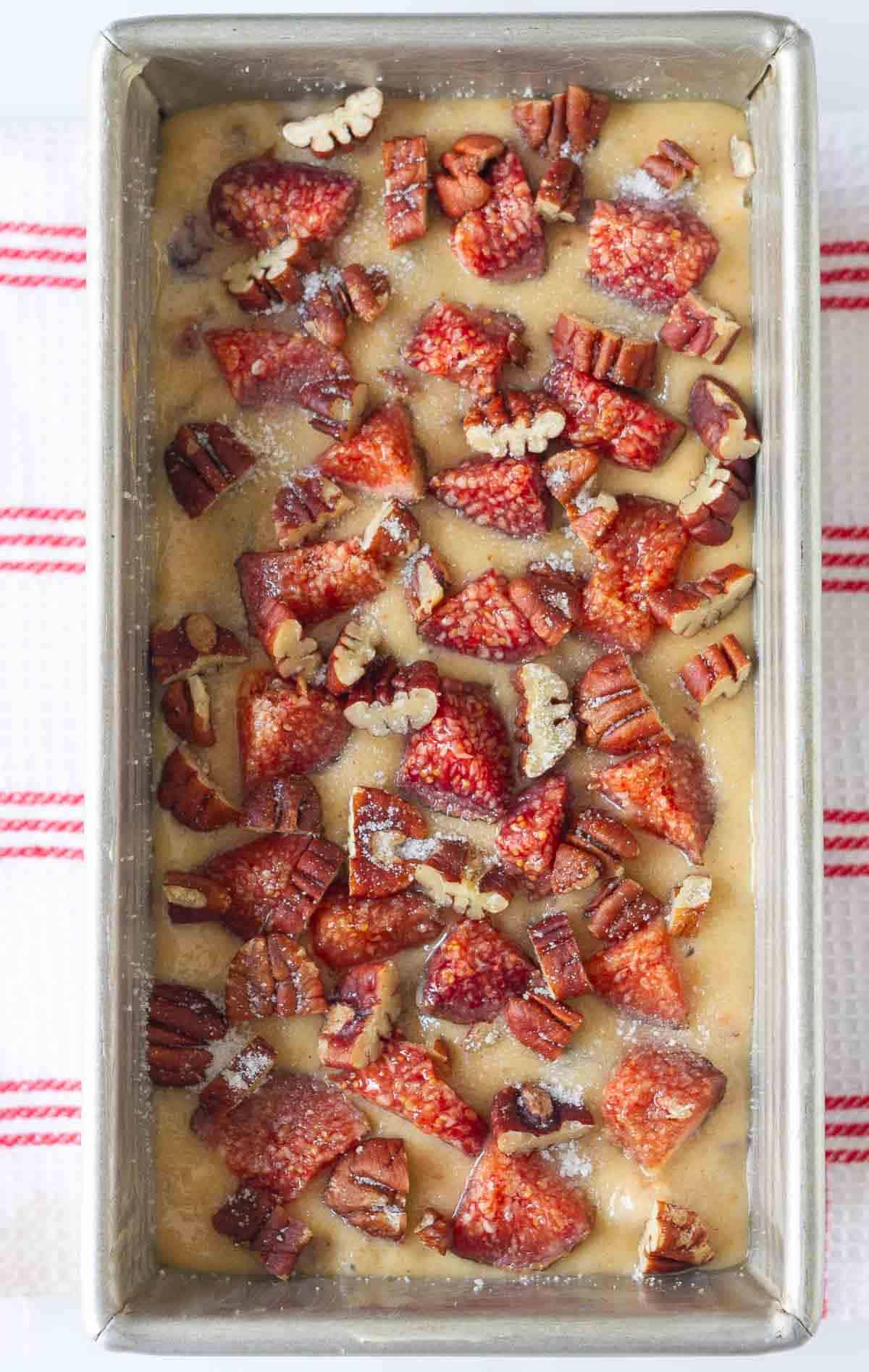 fig bread batter in a loaf pan topped with chopped figs and pecans.