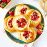 Strawberry cream cheese rolls stacked on a cake stand with strawberries on the side.