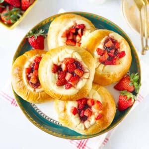 Strawberry cream cheese rolls stacked on a cake stand with strawberries on the side.