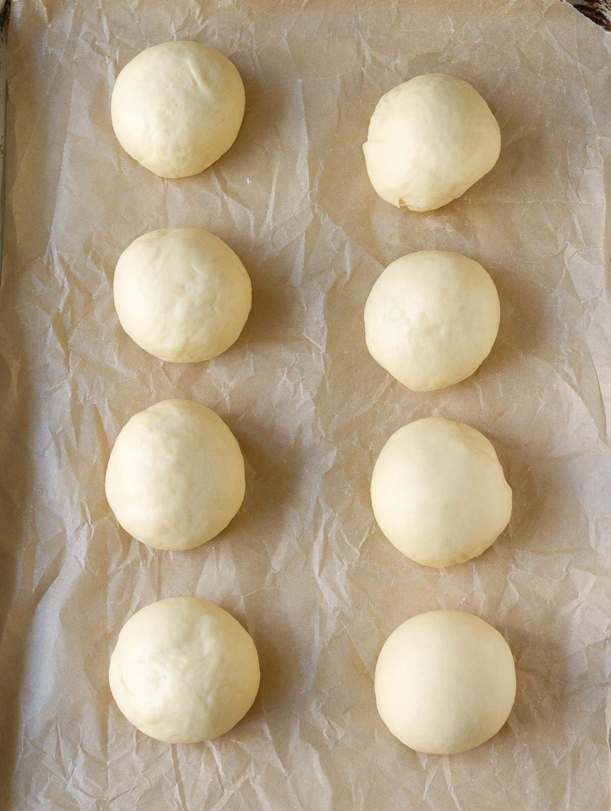 Proofed dough balls on a paper-lined baking tray.