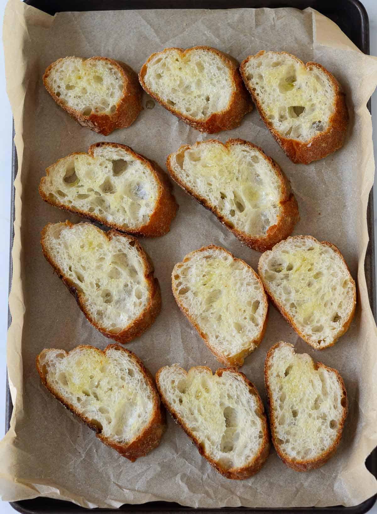 Sliced baguette on a parchment-lined tray.