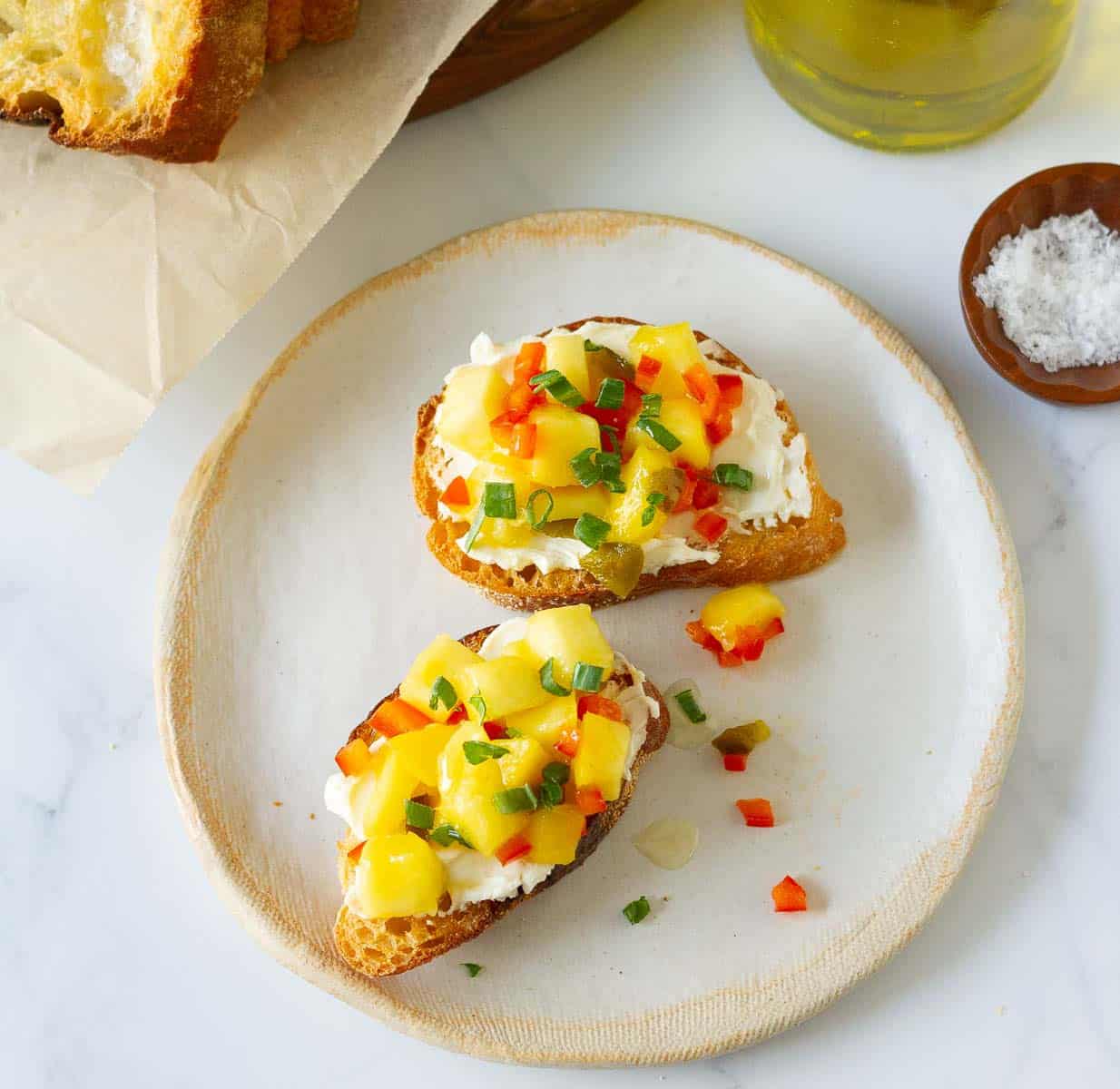 2 pieces of crostini topped with mango topping on a small plate.