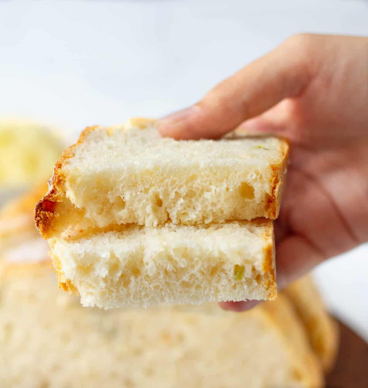 A hand holding a slice of bread cut into 2 to show texture.