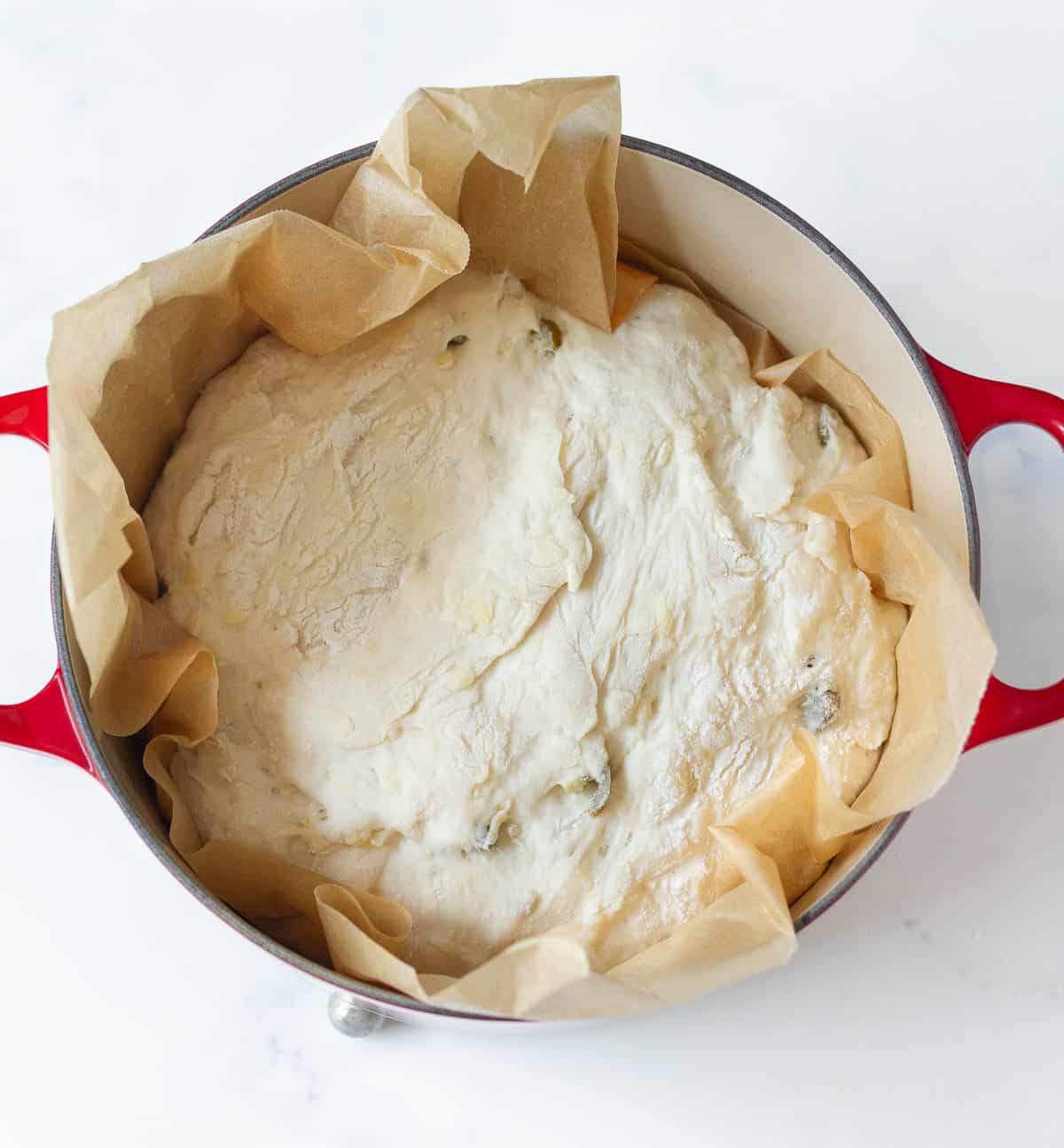 Bread dough on parchment paper in a Dutch oven.