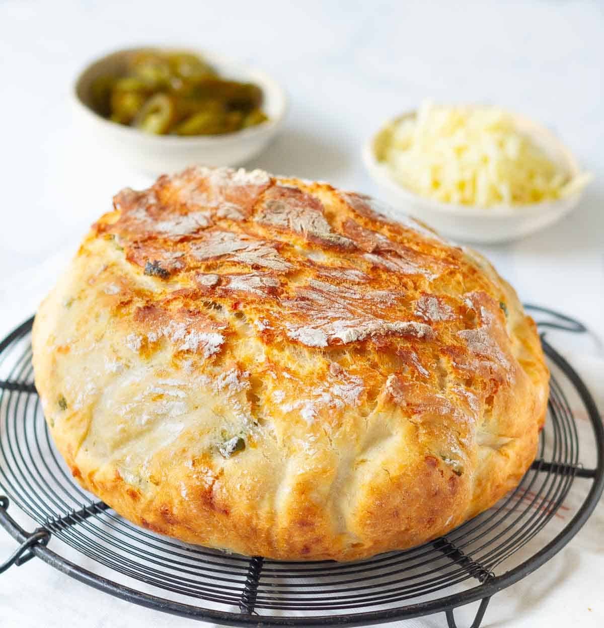 A loaf of no-knead bread on a wire rack with ingredients around.