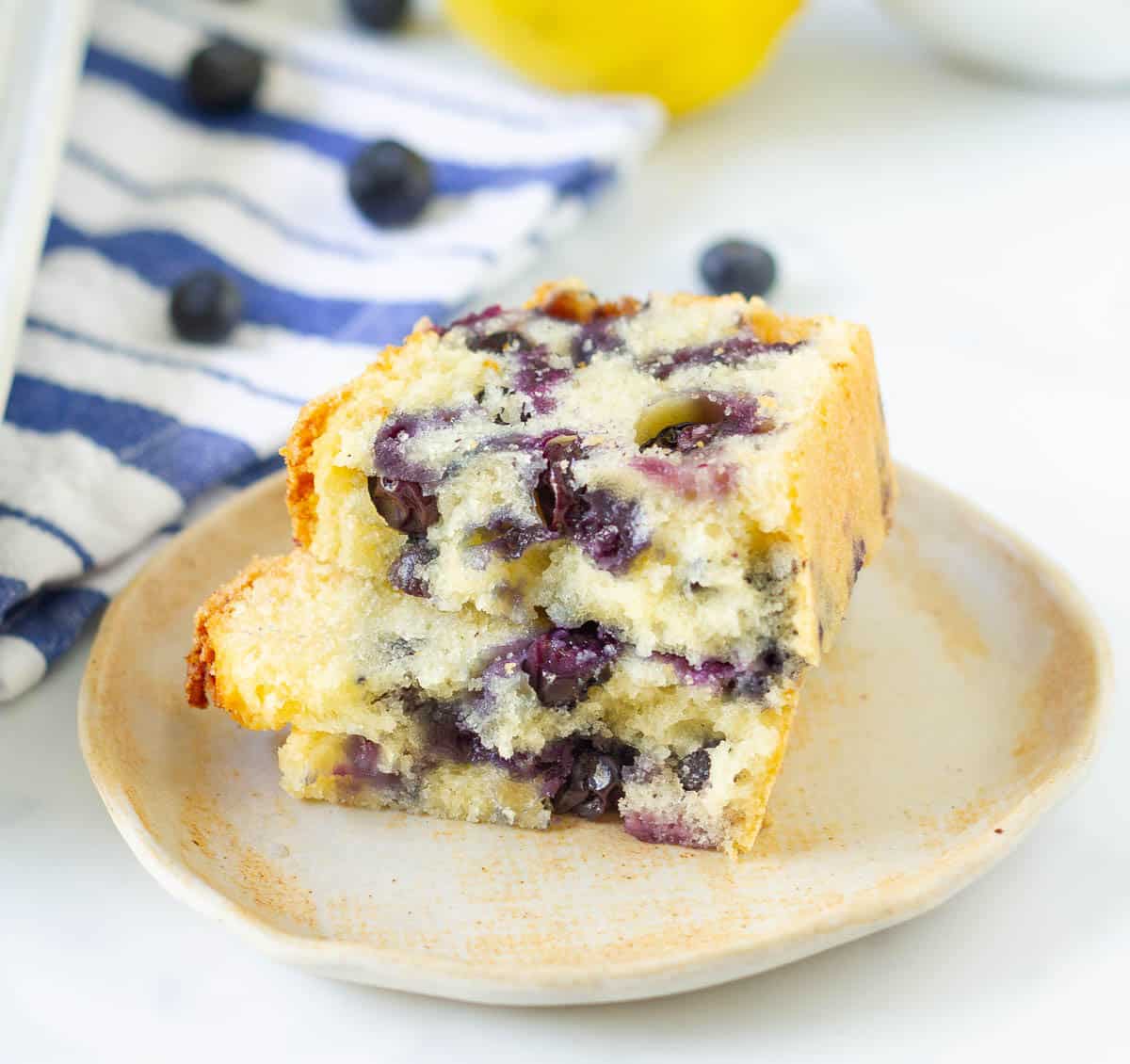 2 halves of a blueberry bread slice stacked on a small plate.