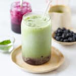 Blueberry matcha latte in a glass with blueberry syrup and blueberries in the background.