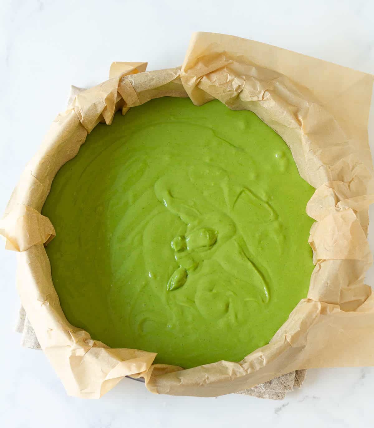 Matcha cheesecake batter in a parchment lined cake pan.