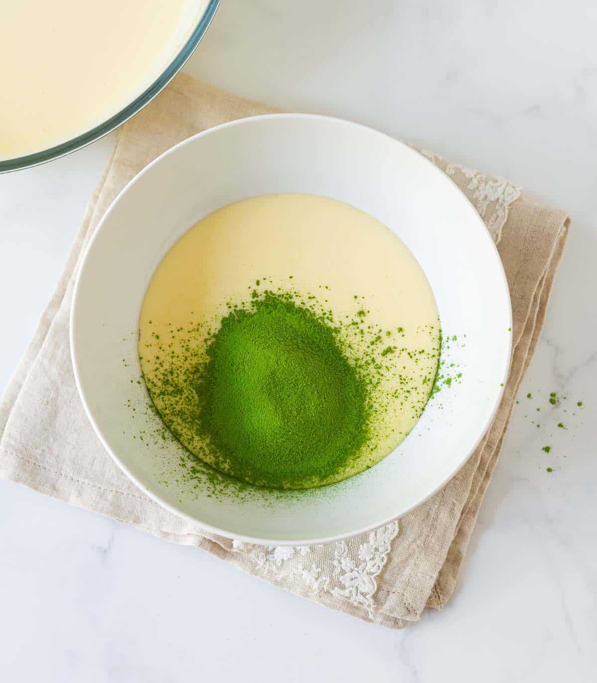 Matcha powder on cream cheese mixture in a bowl.