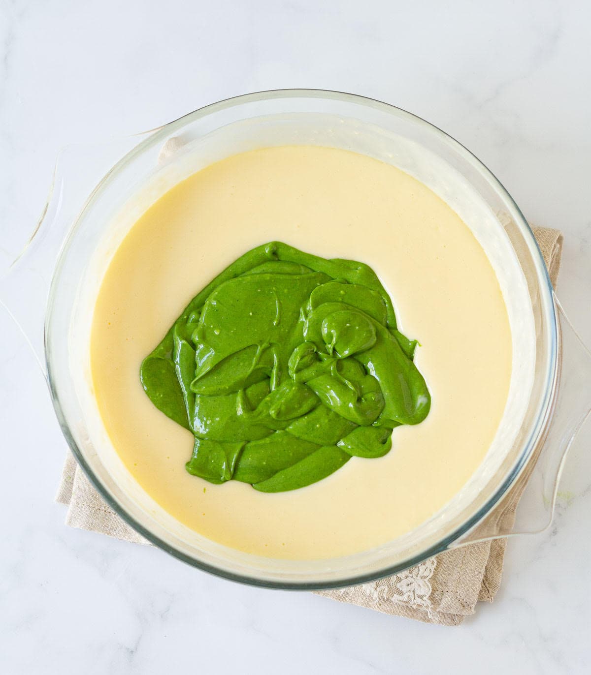 Matcha cheesecake batter on plain cheesecake batter in a bowl.