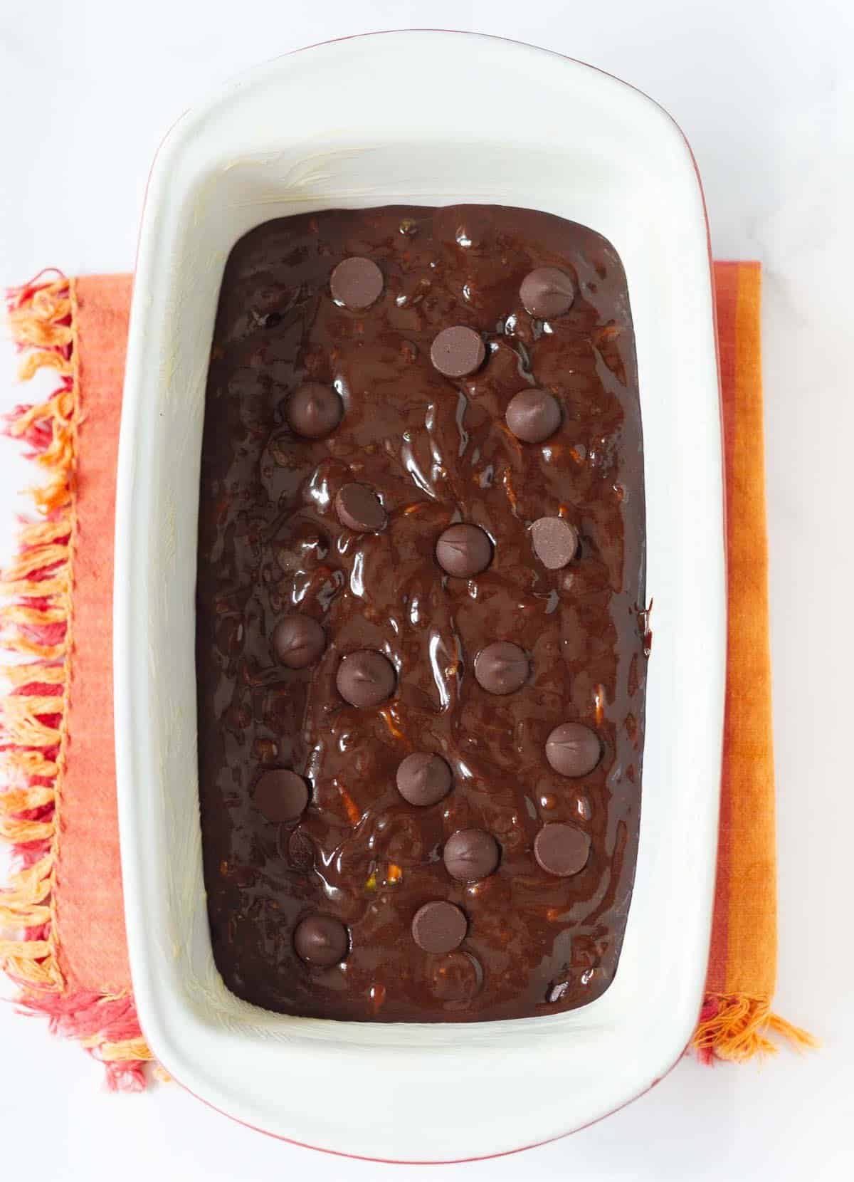 Chocolate zucchini bread batter with chocolate chips on top in a cake pan.